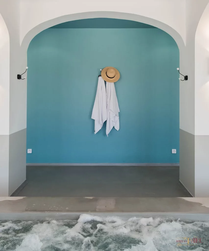 Mur turquoise du spa de l’Hôtel du Parc à Hossegor avec peignoir blanc et chapeau de paille suspendus, au bord d’un bassin de balnéothérapie
